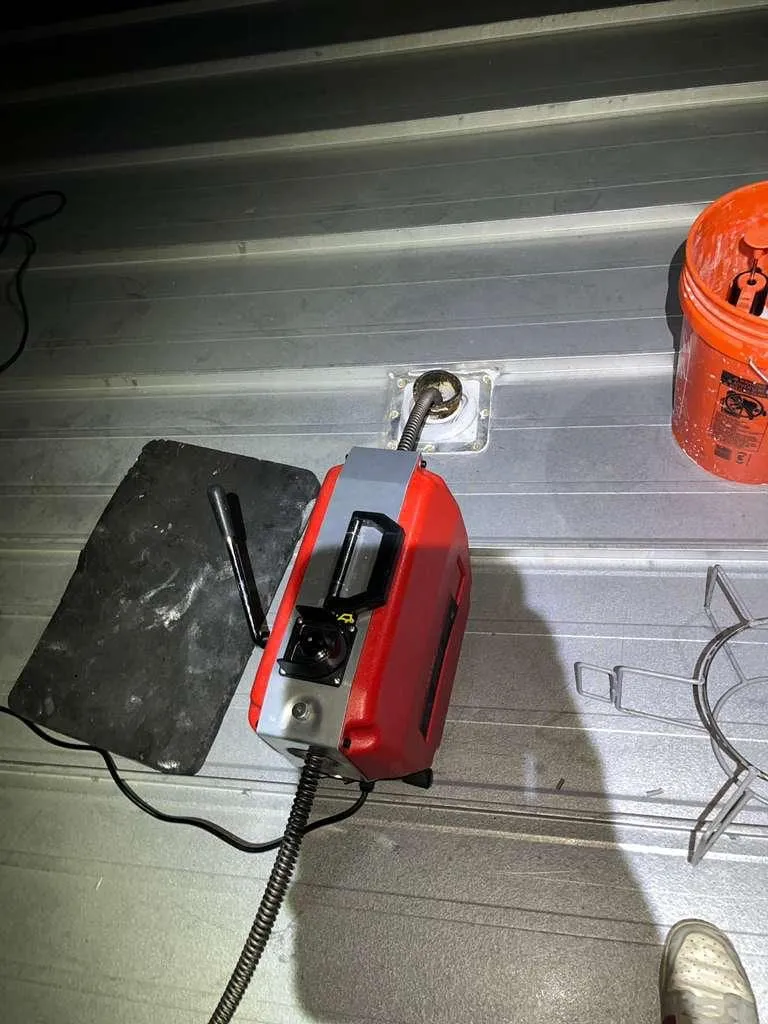 A compact drain machine set against a wall opening with its cable entering the line