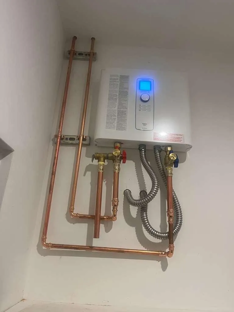 A tankless water heater glowing with its blue status light over tidy copper runs strapped to the wall